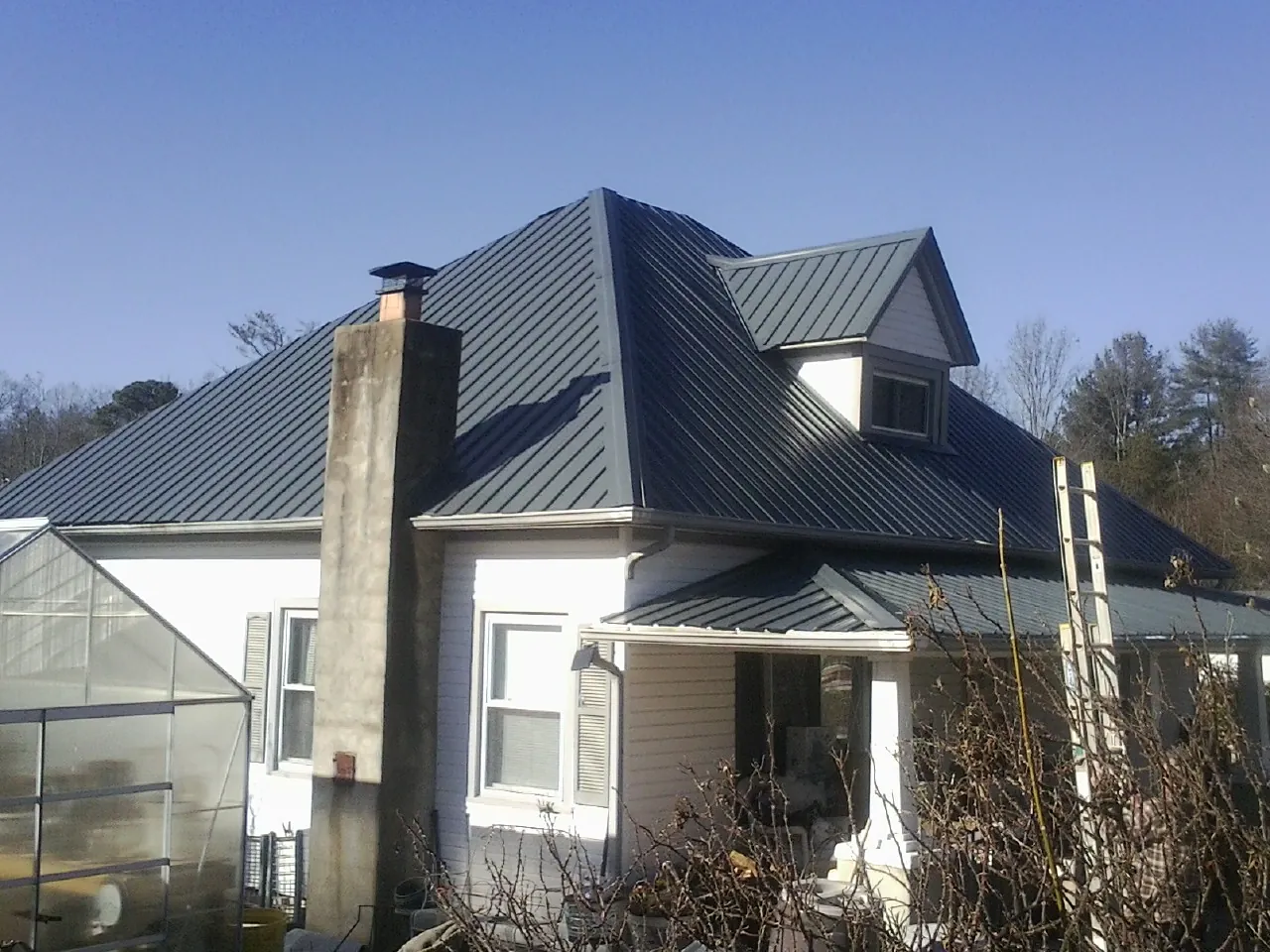 Dark blue standing seam metal roof on a white farmhouse with dormer — Slate & Tile Roof Repair by Roofing Brothers in Evanston