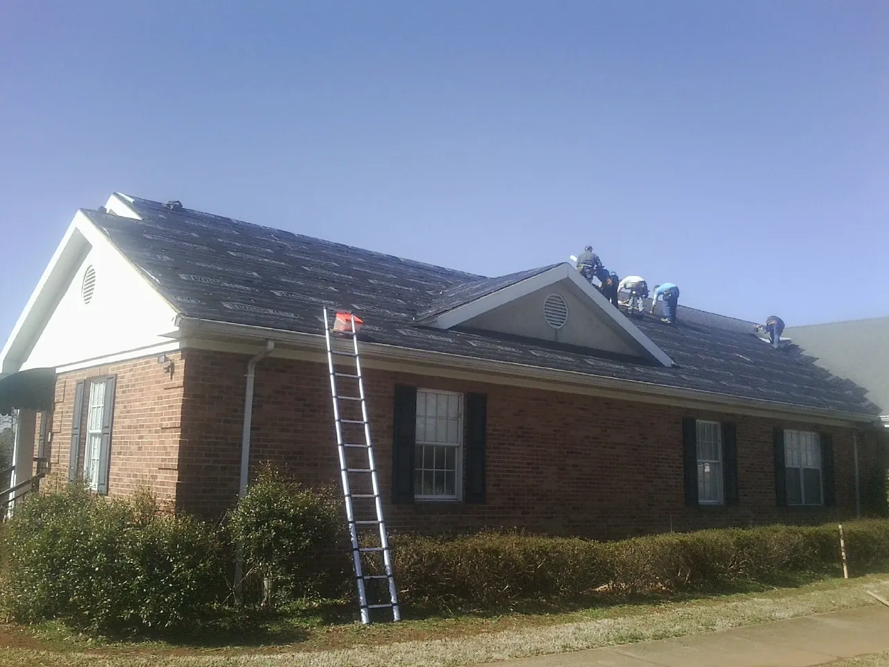 Crew tearing shingles off a brick ranch roof with a ladder set — Emergency Roof Repair work by our crew in Evanston