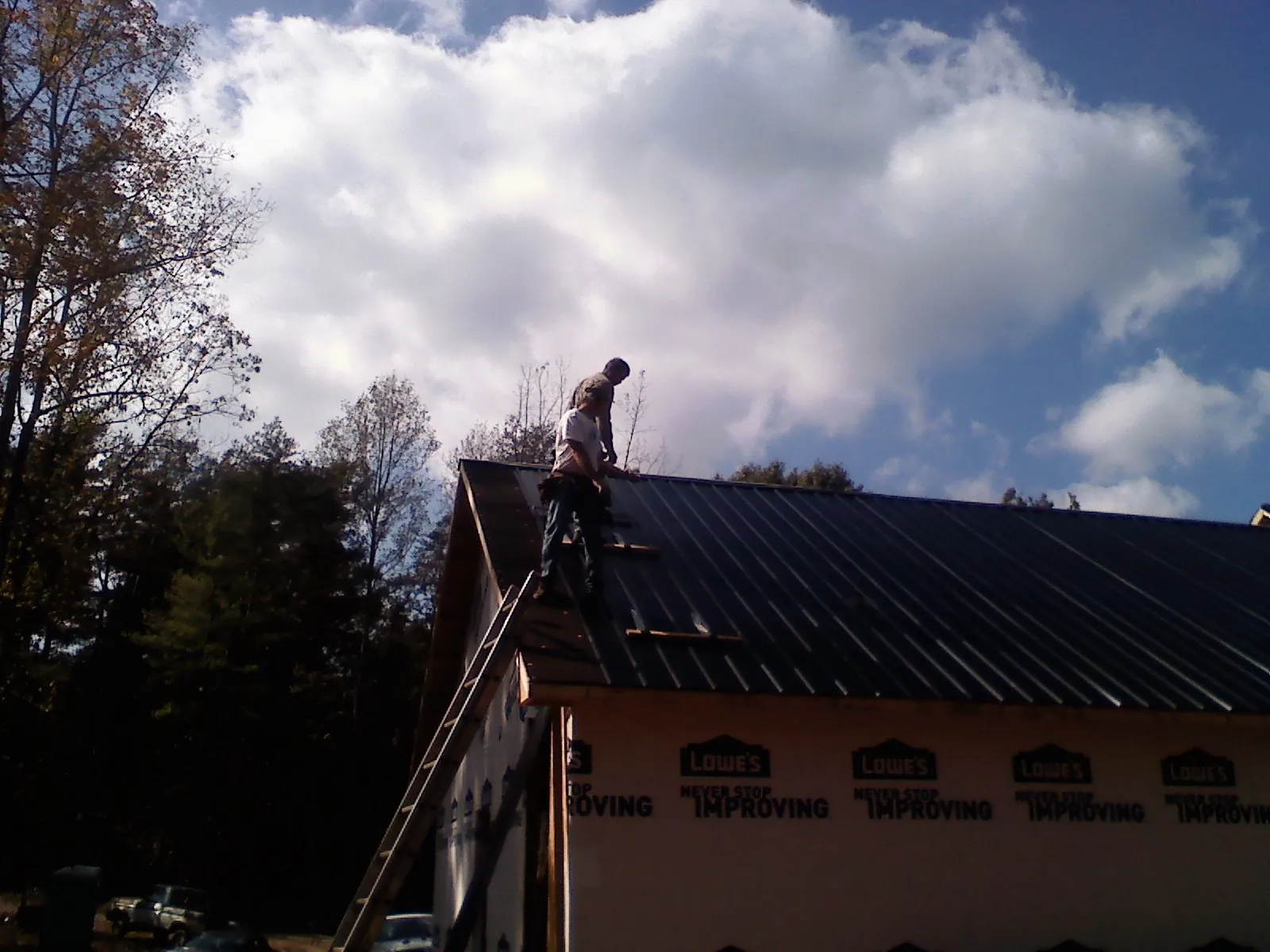 Roofer fastening dark metal panels high against a cloudy sky, from a Roof Inspection job in Evanston
